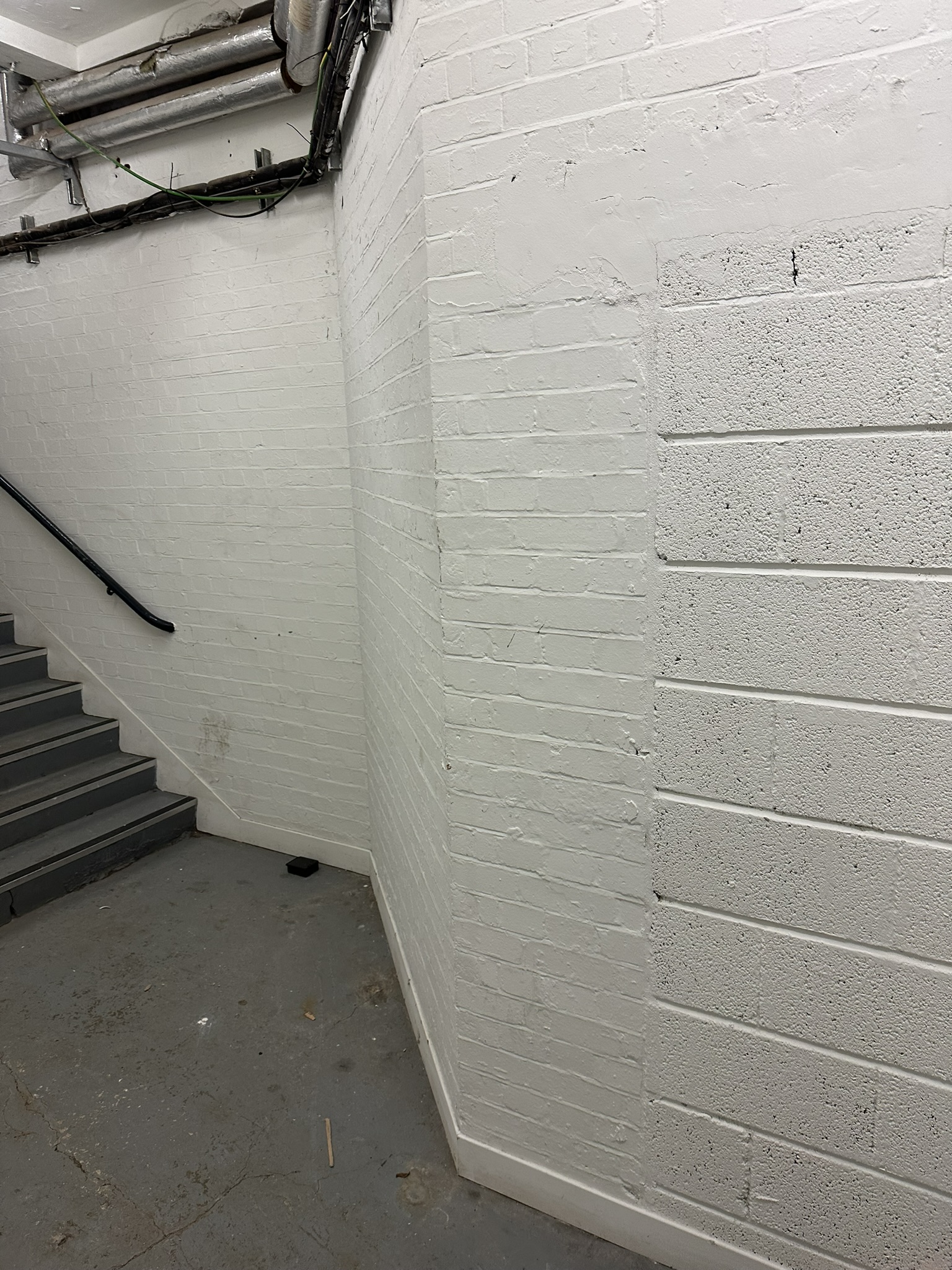 Indoor stairwell and landing with white walls and a handrail.