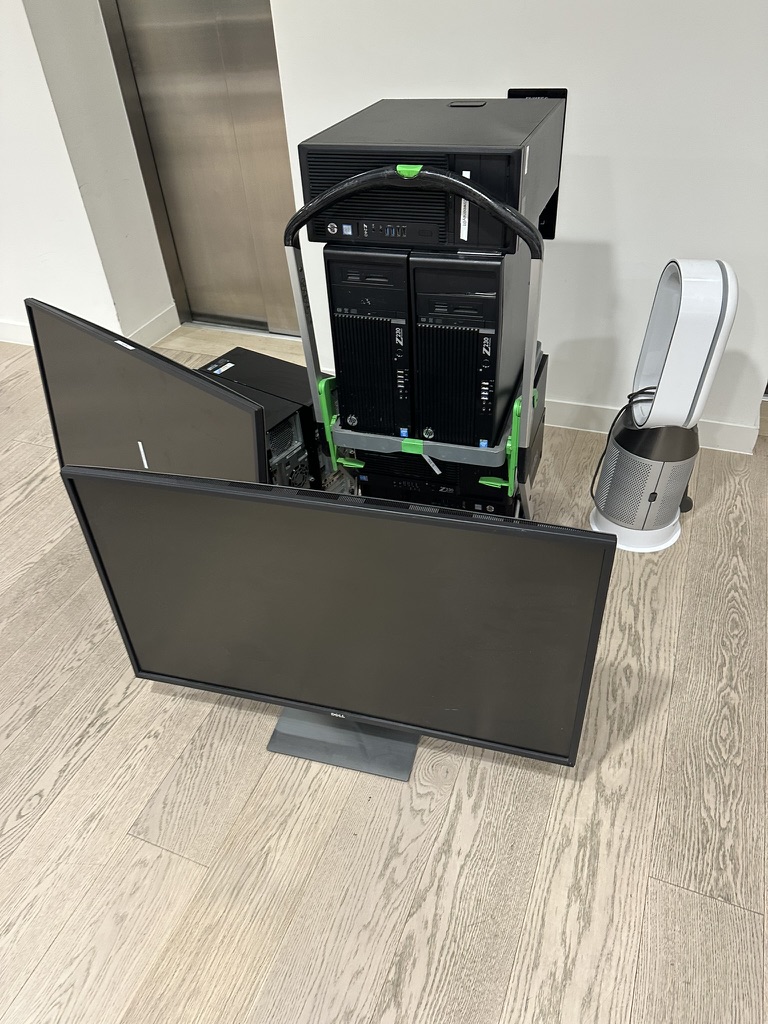 Computer towers on a trolley beside monitors and a fan, prepared for WEEE collection